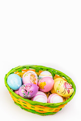 Wicker basket with Easter eggs hand painted on white tabletop background