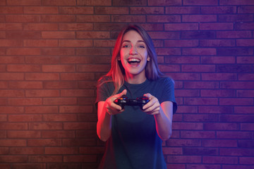Emotional young woman playing video games with controller near brick wall © New Africa