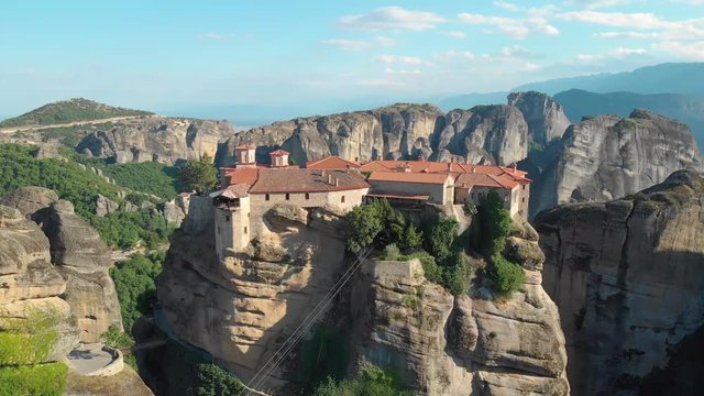 DRONE: Stunning aerial view of a religious village built on top of a high cliff in the picturesque continental Greek countryside. Round boulders surround the world famous Orthodox Christian monastery.