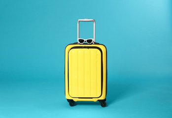Stylish suitcase with sunglasses on color background