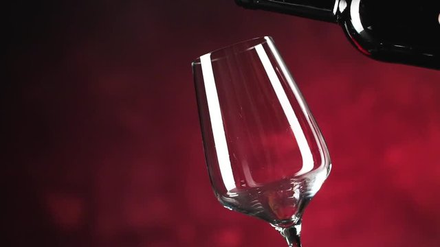 Wein. Rotwein, der in Weinglas &uuml;ber dunklem Hintergrund gie&szlig;t.