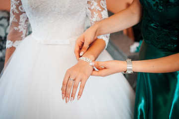 Bridesmaid helps to wear bracelet on the brides hand