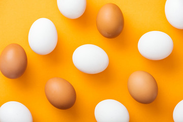top view of whole white and brown fresh chicken eggs on bright orange background