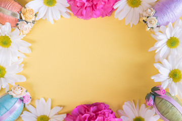 Fototapeta na wymiar Flat lay frame of Easter eggs and flowers on solid pastel yellow background