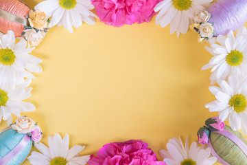 Fototapeta premium Flat lay frame of Easter eggs and flowers on solid pastel yellow background