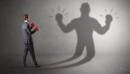 Fototapeta premium Businessman trying to fight with his unarmed shadow 