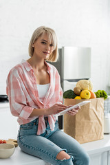 attractive woman using digital tablet near paper bag with ingredients