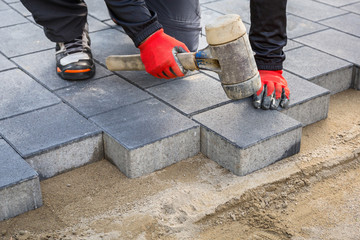 Hands of worker installing concrete paver blocks with rubber hammer