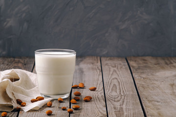 Organic vegan nut milk in glass with almond nuts on wooden table on grey background, copy space. Vegan alternative food, clean eating concept.