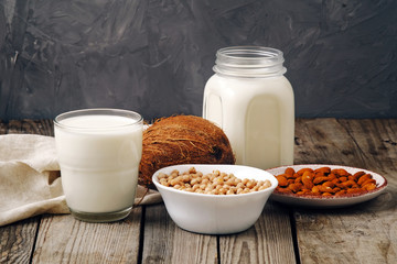 Glass cup and jar of vegan plant milk and almonds, nuts, coconut, soya milk on wooden table. Dairy free milk substitute drinks and various ingredients, vegan food, lactose free concept