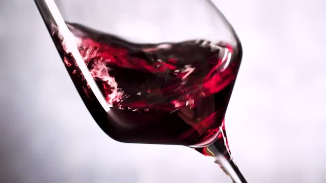 Wein. Rotwein, der in Weinglas &uuml;ber dunklem Hintergrund gie&szlig;t.