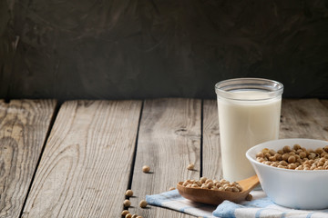 Healthy organic soy milk dairy free alternative in cup and bowl with soybean on dark wooden background. Vegan milk lactose free concept.