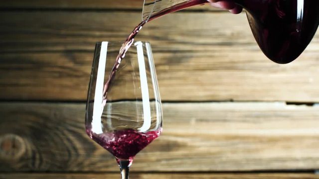 Wein. Rotwein, der in Weinglas &uuml;ber dunklem Hintergrund gie&szlig;t.