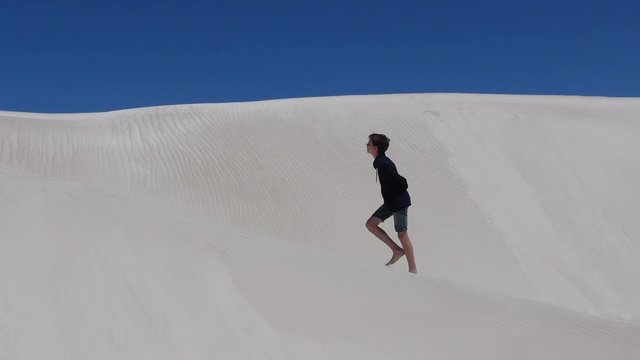 Tenage boy walking up a huge white sand dune, thirsty, exhausted, tired