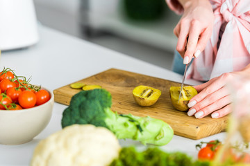 cropped view of girl cutting kiwi fruit near ingredients in kitchen