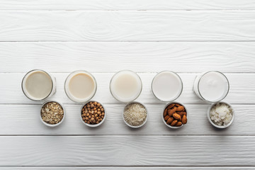 top view of glasses with coconut, chickpea, oat, rice and almond milk with ingredients in bowls