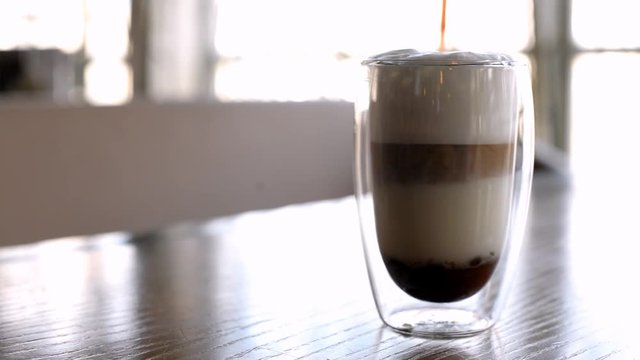 The process of making coffee latte in a stelean glass on a table in a restaurant with caramel toping, espresso poured into milk