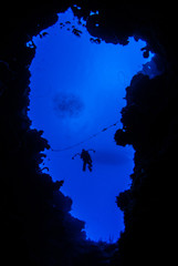 A silhouette shot of a scuba diver with an underwater camera in his hand descending into the abyss....