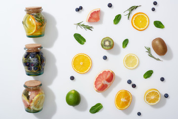 top view of detox drinks in jars near fruit slices, blueberries, mint and rosemary