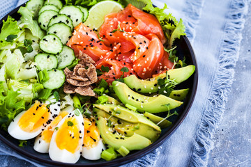 Salmon poke bowl served with avocado, eggs, cucumber and greens