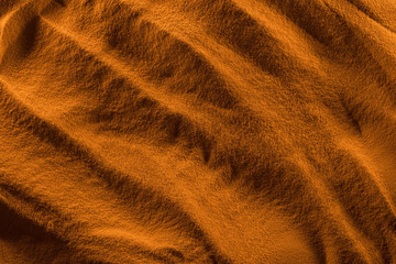 top view of textured sand with smooth waves and orange color filter