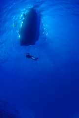Fototapeta premium A silhouette shot of divers returning to a dive boat. The water is very clear and the sun can be seen behind the dive boat.