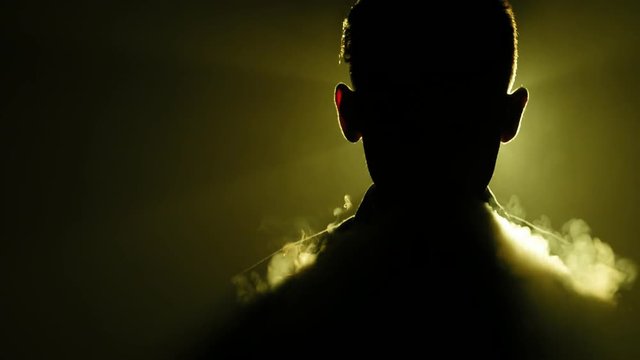 Silhouette of young boy smoking electronic cigarette in the darkness. 