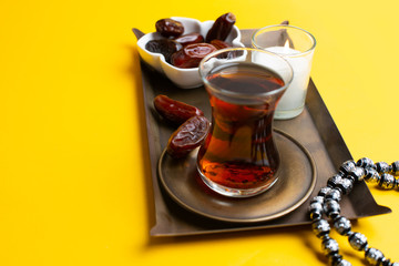 Ramadan Kareem Festival, close up of dates at bowl with rosary and cup of black tea on yellow background.