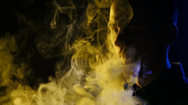 Silhouette of vaping man in the darkness. Boy blowing O's with vapor from e-cigarette. Vape tricks