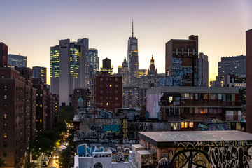 The colorful lights of the NYC skyline shine as evening falls on the buildings and streets of...