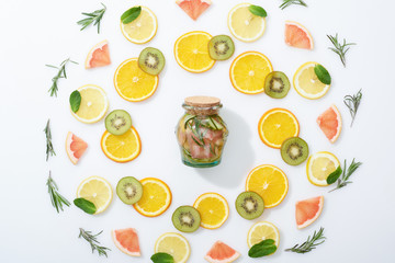 flat lay with sliced kiwi, oranges, lemons, grapefruits, mint, rosemary and fresh detox drink in jar on grey background