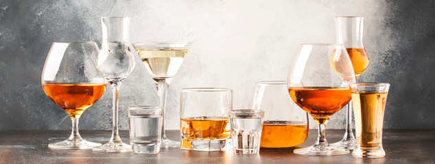 Set of hard strong alcoholic drinks and spirits in glasses in assortment: vodka, cognac, tequila, brandy and whiskey, grappa, liqueur, vermouth, tincture, rum. Gray bar counter background