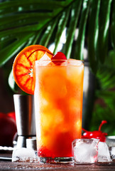 Classic tequila sunrise cocktail with silver tequila, grenadine syrup, orange and ice cubes. Wooden bar counter in the bar. Summer mood concept. Selective focus. Copy spac