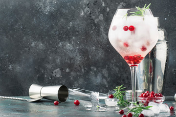Cranberry cocktail with ice, fresh rosemary and red berries in big wine glass, bar tools, gray bar counter background, copy space, selective focus