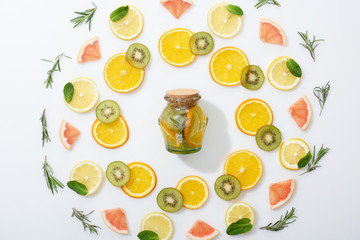 top view of sliced kiwi, oranges, lemons, grapefruits, mint, rosemary and detox drink in jar on grey background