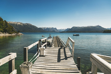 Landscape photo with old wooden pier, transparent lake water, and mountains. Concept of travel, lifestyle, harmony, summer, and vacations