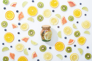 top view of organic detox drink in jar among sliced fruits and blueberries on white background