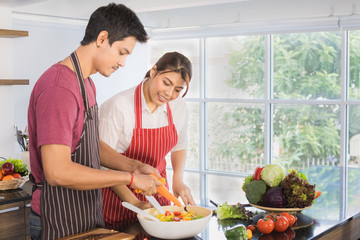 Portrait of happy young Asian couple sharing a good times prepare healthy salad, slicing carrot...