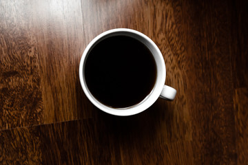 Black coffee in white cups by hand on wooden floors and coffee beans