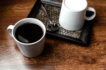 Black coffee in white cups by hand on wooden floors and coffee beans