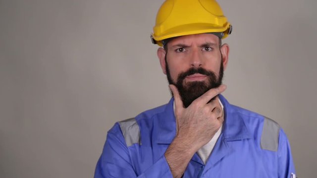 Thoughtful bearded middle age man in hard hat in the helmet touching his beard and thinking thoughts with smart face, expressing question and doubt