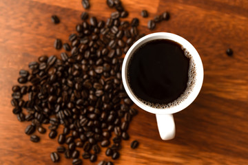 Black coffee in white cups by hand on wooden floors and coffee beans
