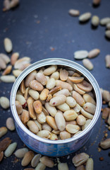Salty peanut kernels in metal jar. Roasted and dried on black background. Top above view. Close up. Peeled. Snack with protein