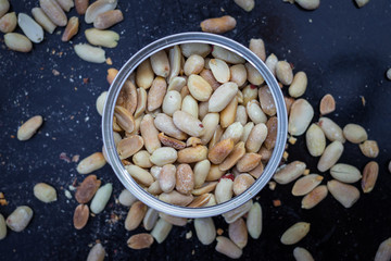 Salty peanut kernels in metal jar. Roasted and dried on black background. Top above view. Close up. Peeled. Snack with protein