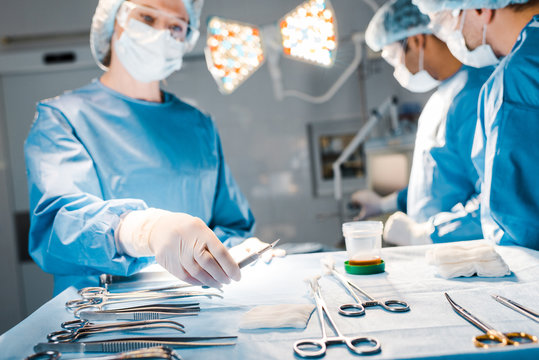 selective focus of doctors doing operation and nurse in uniform and medical cap holding scalpel