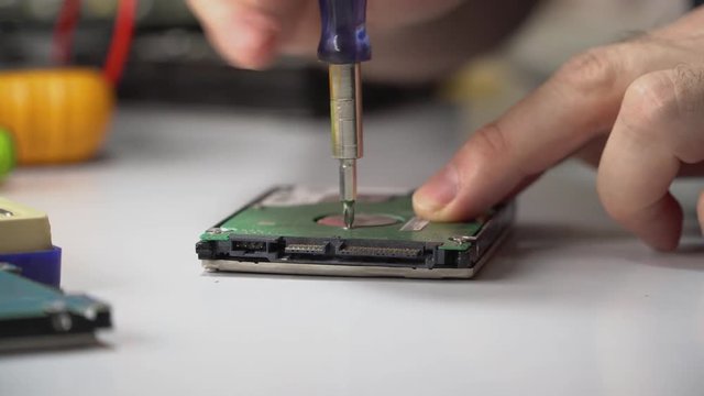 electronic engineer repairs computer hard drive. technologist with a screwdriver disassembles hdd