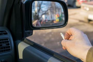 close-up, male hand holding a cigarette in a car that stands on the parking lot in a residential area