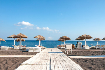 Fototapeta premium Beautiful view of the Mediterranean Sea from the sandy beach of the island of Crete. On the beach, people sunbathe on the lounge chairs