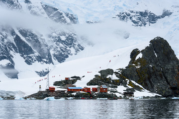 View of the Almirante Brown Station from the water, line of tourists hiking in the background,...