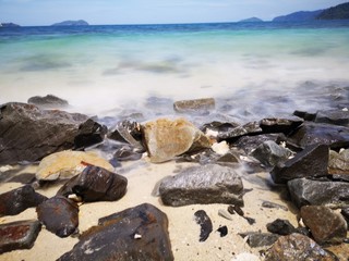 The beautiful silky smooth water waves and rocks on the sea shore during the sunny day.
